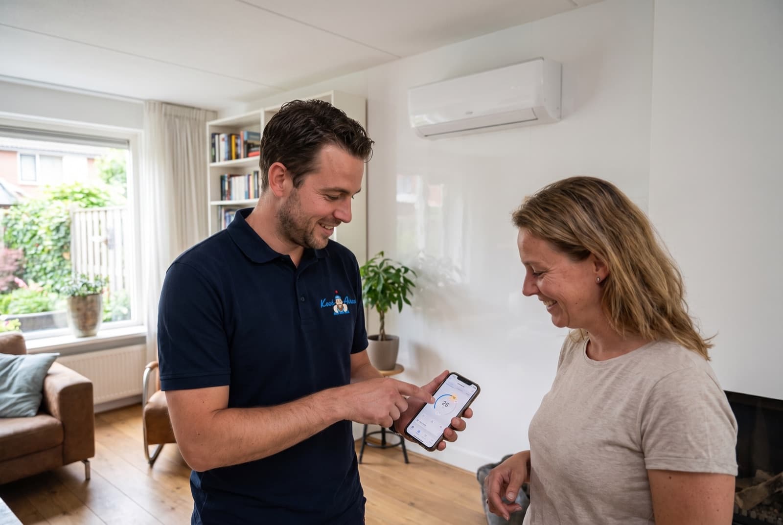 Monteur van Keesairco legt de bediening via de app uit bij een airco in de woonkamer